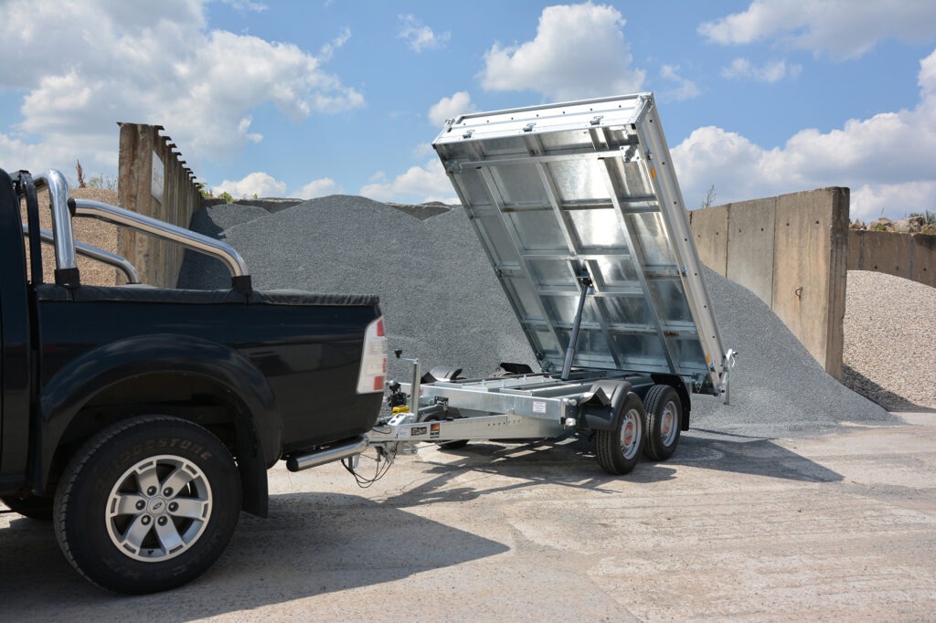 Black Pickup Truck with a Dual axle Metal Dump Trailer Whose Bed is Raised Dumping Gray Gravel at a Quarry or Yard Site