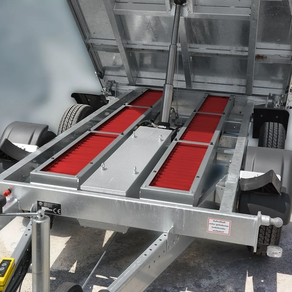 Metal trailer frame with red bristle rollers and a hydraulic piston, likely a conveyor system on a trailer used for loading or cleaning equipment