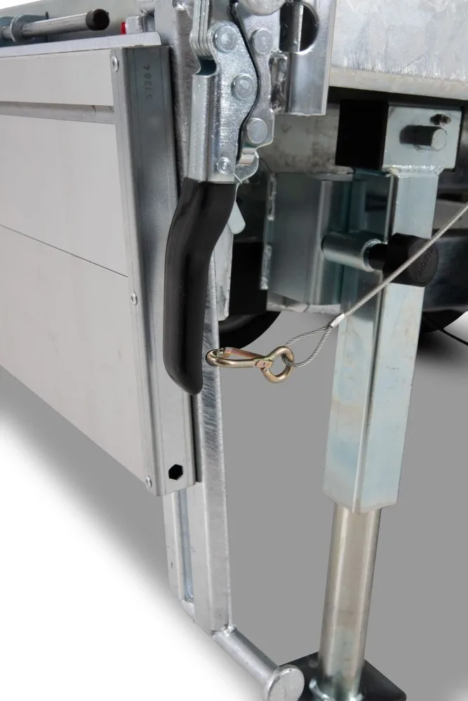 Close-up of a metal gate latch with a black grip, secured by a steel cable and brass ring on an industrial frame.