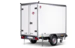 White enclosed cargo trailer with double rear doors, stabilizing legs down, and a single axle beneath a metal frame.