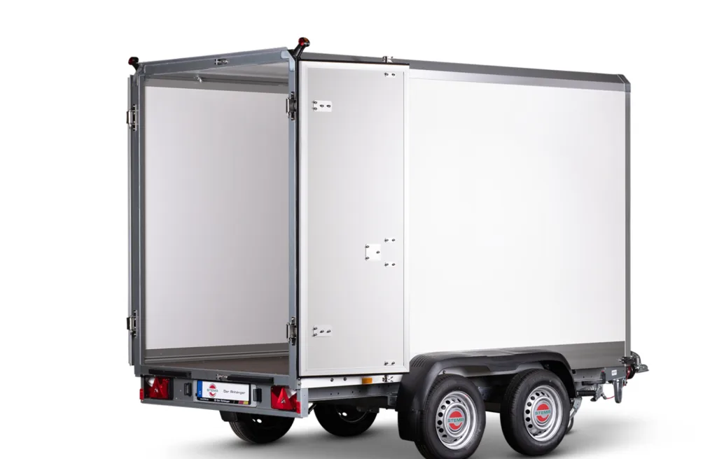 Silver cargo trailer with rear doors open, showing a large white interior, mounted on a dual-axle chassis with red taillights and a small license plate area at the back.