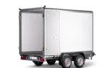 Silver cargo trailer with rear doors open, showing a large white interior, mounted on a dual-axle chassis with red taillights and a small license plate area at the back.