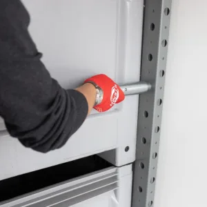 Worker wearing a red glove inserts or removes a metal locking pin into a shelving upright on a gray rack.