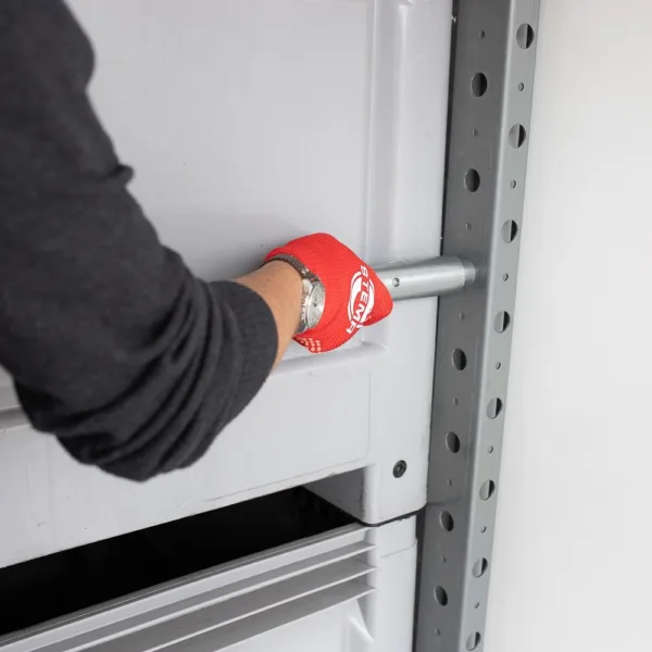 Worker wearing a red glove inserts or removes a metal locking pin into a shelving upright on a gray rack.